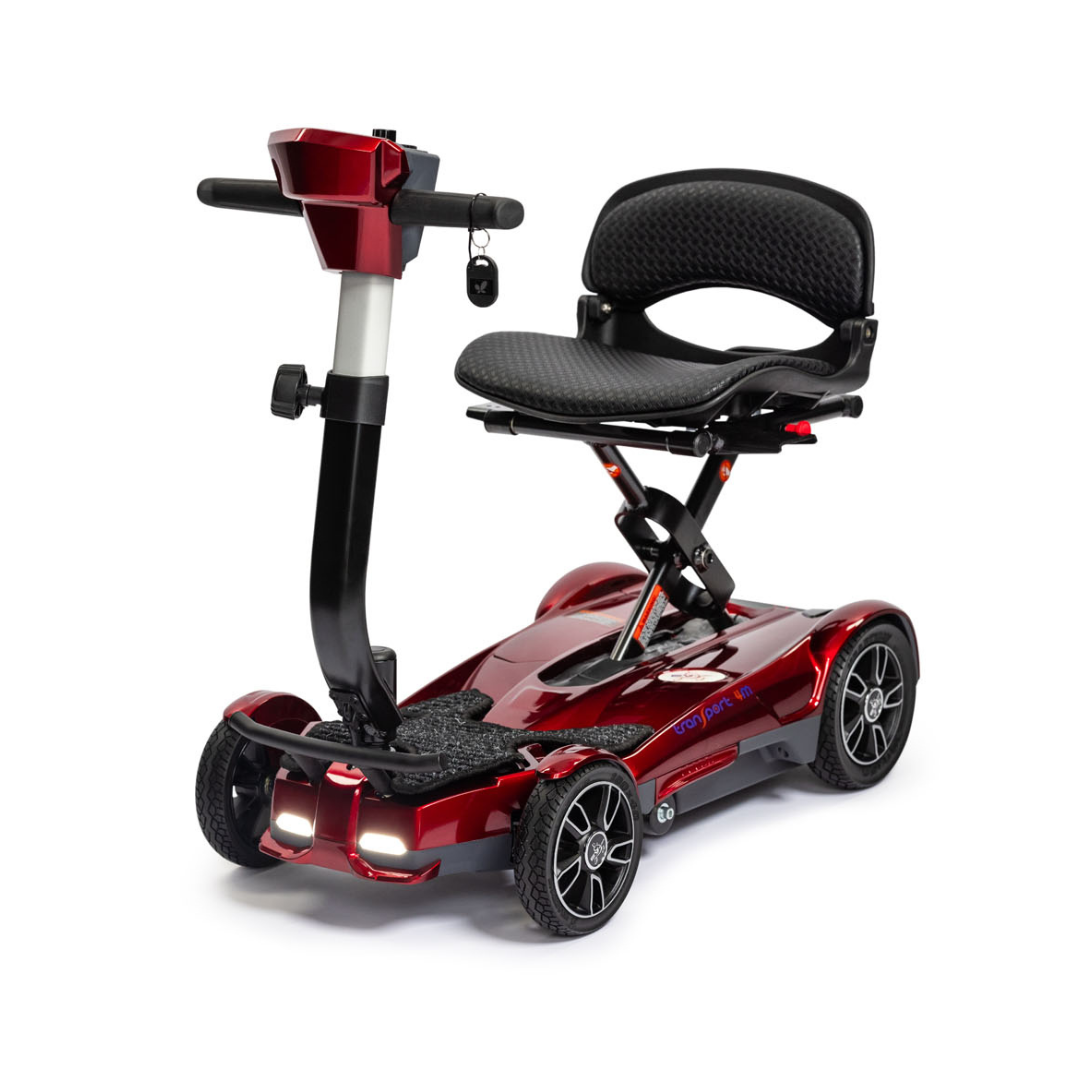 The EV Rider Transport 4M Travel Scooter is a compact, red, four-wheel scooter with a black cushioned seat, handlebars, and front lights—ideal for personal transportation and enhanced accessibility.